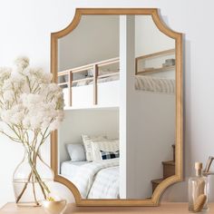 a mirror sitting on top of a table next to a vase with flowers in it