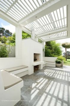 an outdoor fireplace in the middle of a patio with white walls and ceiling beams, surrounded by greenery