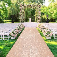 an outdoor ceremony setup with white chairs and pink flowers on the aisle, surrounded by greenery