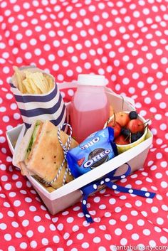 a lunch box filled with sandwiches, fruit and juice on a polka dot tablecloth