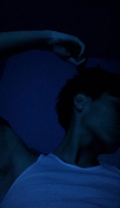 a man laying in bed at night with his hand on his head and arm behind him