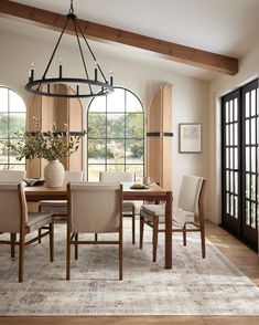 a dining room table with chairs and a vase on top of it in front of large windows