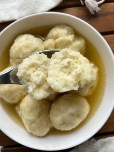 a white bowl filled with dumplings sitting on top of a wooden table next to a spoon