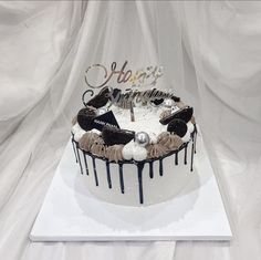 a birthday cake with white frosting and black icing dripping down the side on a white surface