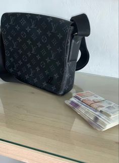 a black louis vuitton bag sitting on top of a table next to money