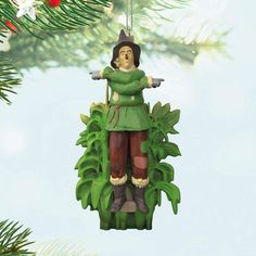 a christmas ornament hanging from a tree with green leaves and a person wearing a hat