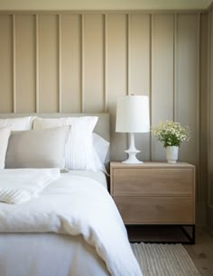 a white bed sitting next to a night stand with a lamp on top of it