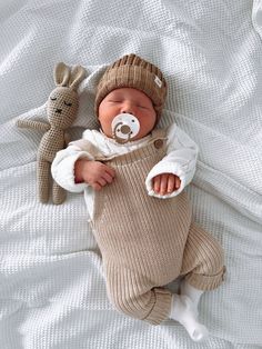 a baby in a knitted outfit laying on a bed next to a stuffed animal