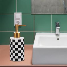 a bathroom sink and soap dispenser in front of a green tiled wall