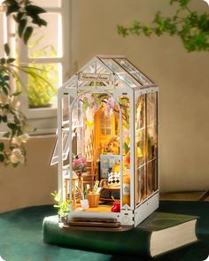 a doll house is sitting on top of a table next to a book and potted plant