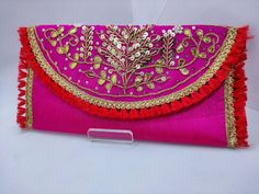 a pink and red clutch bag with gold trimmings on the front, sitting on top of a white surface