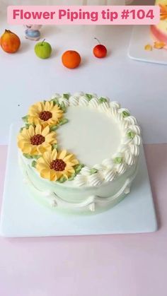 a white cake with sunflowers on it sitting on a table next to fruit