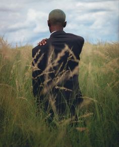 a man in a suit is sitting in the middle of tall grass with his hands on his chest