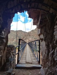 a wooden bridge that is suspended over some rocks and dirt with mountains in the background