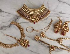 an assortment of gold jewelry on a marble surface with red beads and chains hanging from it