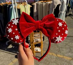 a hand holding up a red minnie mouse ears with white snowflakes on it