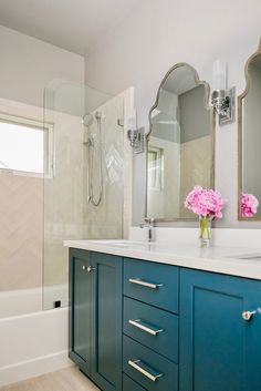 a bathroom with blue cabinets and white counter tops, pink flowers in vase on the sink