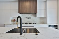 a kitchen with marble counter tops and black faucet, an oven hood over the sink