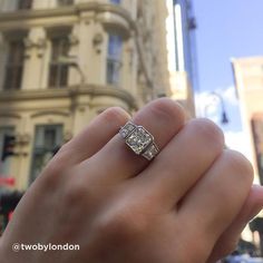 a person's hand holding a diamond ring in front of a building