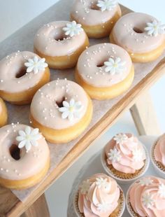 there are many pink frosted donuts on the tray and cupcakes next to it