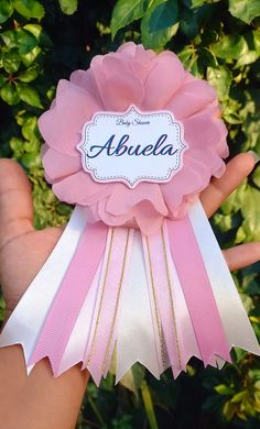 someone holding up a pink ribbon with the name abuela on it in front of some bushes