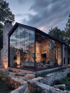 a stone house with glass walls is lit up by the evening sun as it sits on some rocks