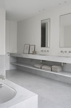 a white bathroom with two sinks, mirrors and a bathtub in the middle of it