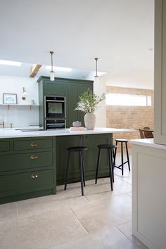 a kitchen with green cabinets and stools in front of the counter top, along with a potted plant