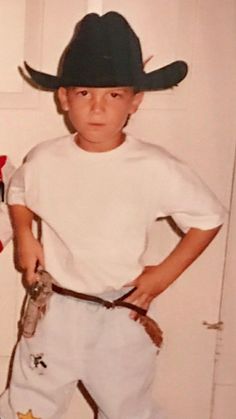 a young boy wearing a cowboy hat and holding a baseball bat in his hand while standing next to a door