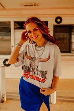 a woman with red hair wearing a gray shirt and blue skirt posing for the camera