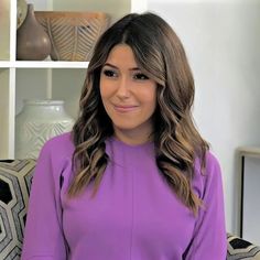 a woman in a purple top is sitting on a couch and smiling at the camera