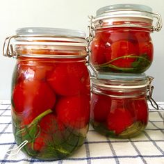 three jars filled with tomatoes sitting on top of a checkered tablecloth covered table