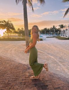 a woman in a green dress is dancing on the sidewalk near palm trees at sunset