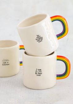 three white mugs with rainbow designs on them sitting in front of the same cup