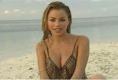 a beautiful woman sitting on top of a sandy beach next to the ocean in a bathing suit