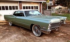 an old green car parked in front of a house next to a fence and driveway