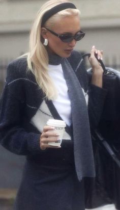 a blonde woman in black and white sweater holding a coffee cup while talking on her cell phone