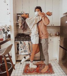 a man and woman standing in a kitchen with their arms around each other, both wearing face masks