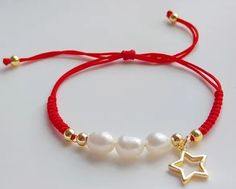 a red string bracelet with white pearls and gold star charms on it, sitting on a white surface