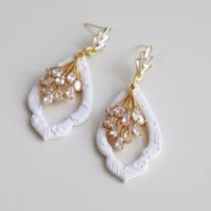 two pairs of white and gold earrings with pearls on the top, one is dangling from a hook