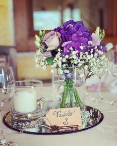 purple and white flowers in a glass vase on a silver tray with a place card