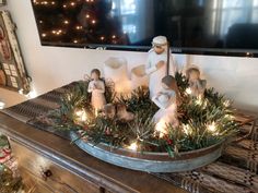 a christmas scene with nativity figurines and lights on a table in front of a flat screen tv