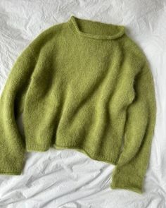 a green sweater laying on top of a white sheet