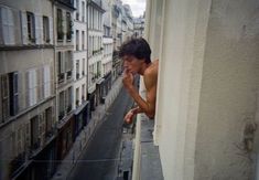 a shirtless man leaning against a wall looking down at the street from an apartment building