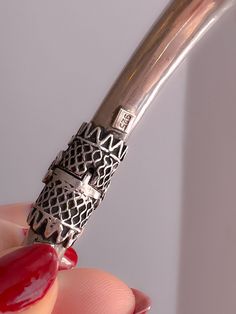 a woman's hand holding a silver pen with red nail polish