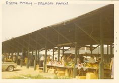 an old photo of people buying fruit and vegetables at a farmers market under a covered area