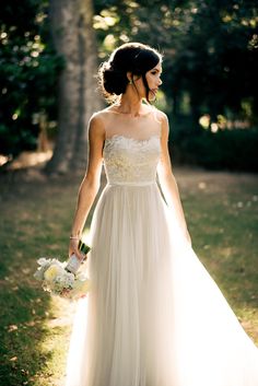 a woman in a wedding dress walking through the grass with her bouquet on her hand