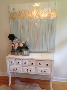 a white dresser with flowers on it in front of a painting