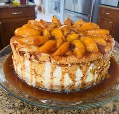 a cake on a glass plate covered in caramel and sliced peaches sitting on top of a kitchen counter