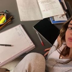 a woman sitting in front of a laptop computer on top of a desk next to a notebook